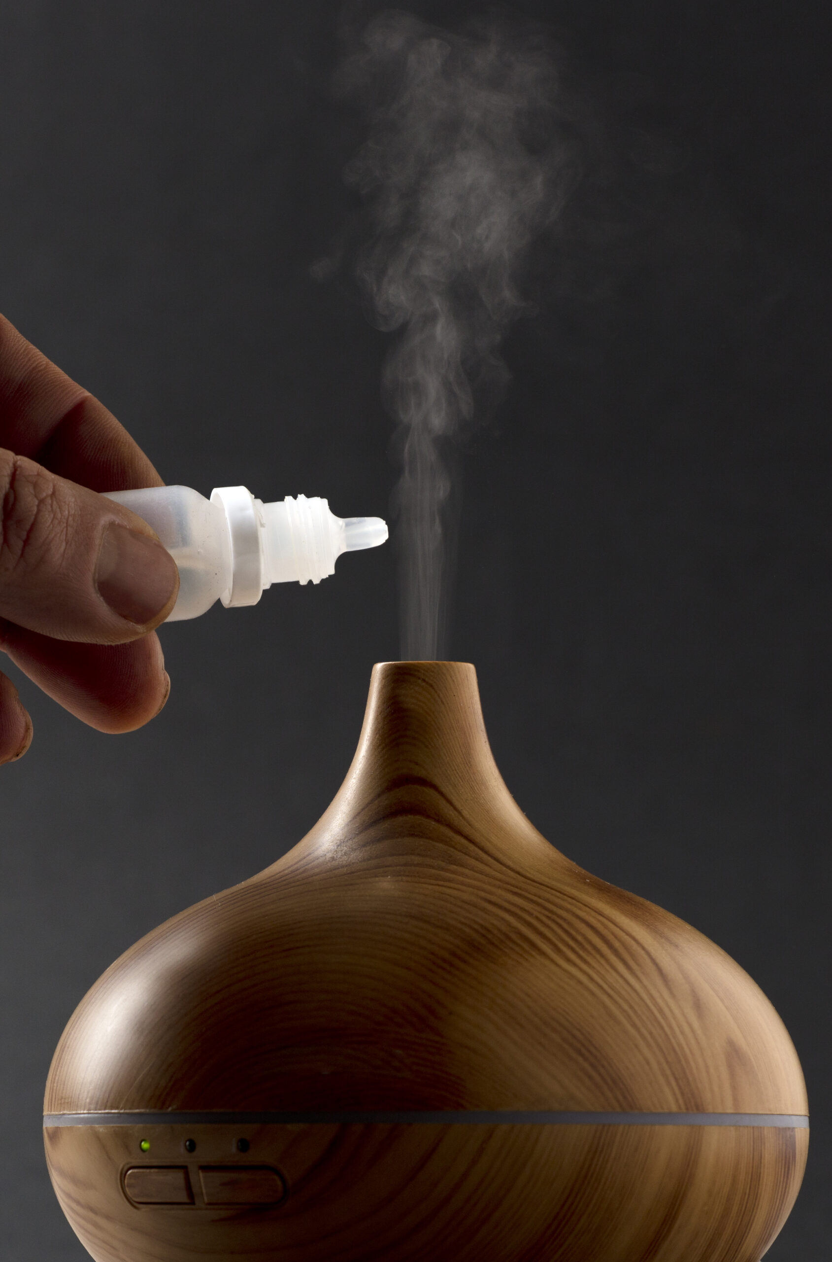 wooden air freshener with steam of natural essences, man’s hand with dispenser, black background